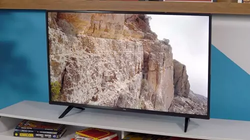 TCL P615 em cima de rack branco, com paisagem de montanha de pedra sendo reproduzida