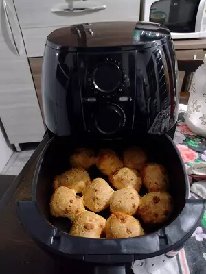 Cadence Pratic Fryer apoiada em mesa de cozinha, com o cesto aberto cheio de pão de queijo