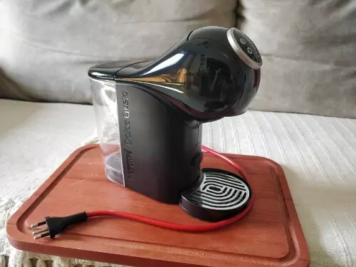 Dolce Gusto Gênio S Plus vista de lado em cima de tábua de madeira sem nenhuma xícara apoiada.