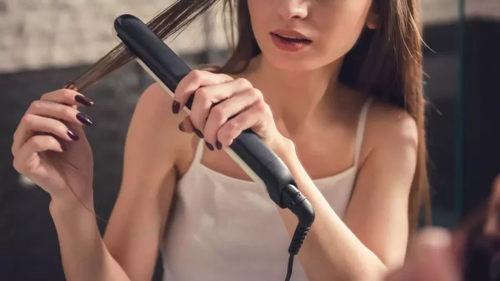 Abertura do post sobre como passar chapinha no cabelo: Mulher usando prancha em frente ao espelho