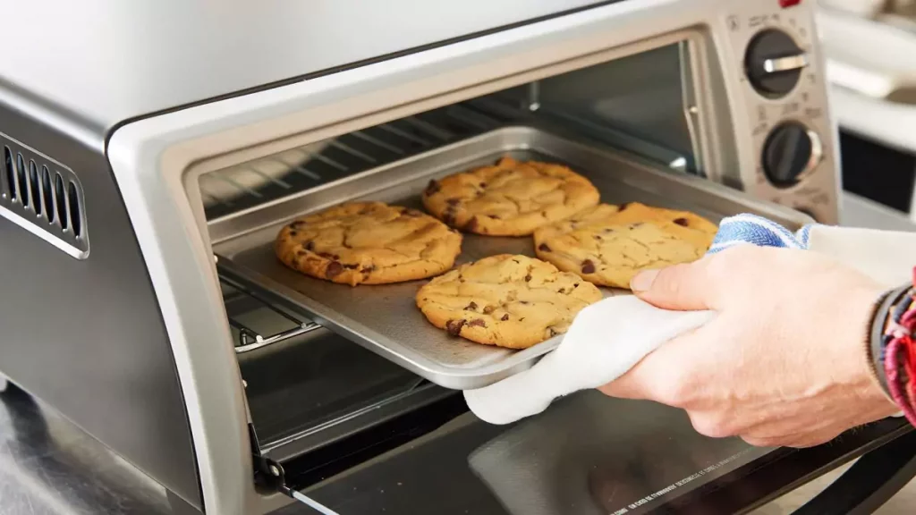 Pessoa manuseando biscoitos com luvas em forninho elétrico