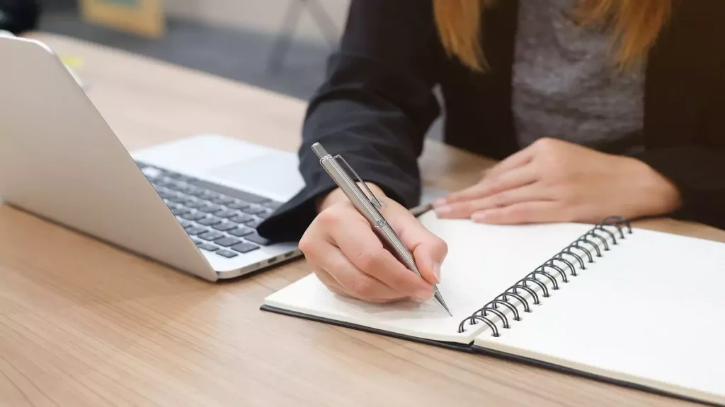 mulher escrevendo ao lado de notebook para estudar